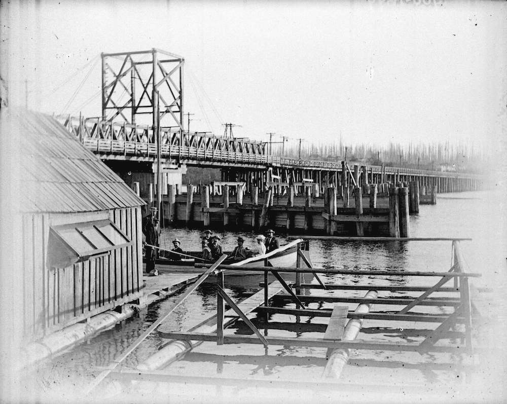 1899-Men and women in boat at Andrew Wallace's boat building shed next to Granville Street Bridge
