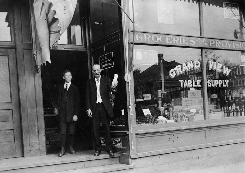 1900-Exterior of Grandview Table Supply, a groceries and provisions store with the proprietor and his young assistant at the door