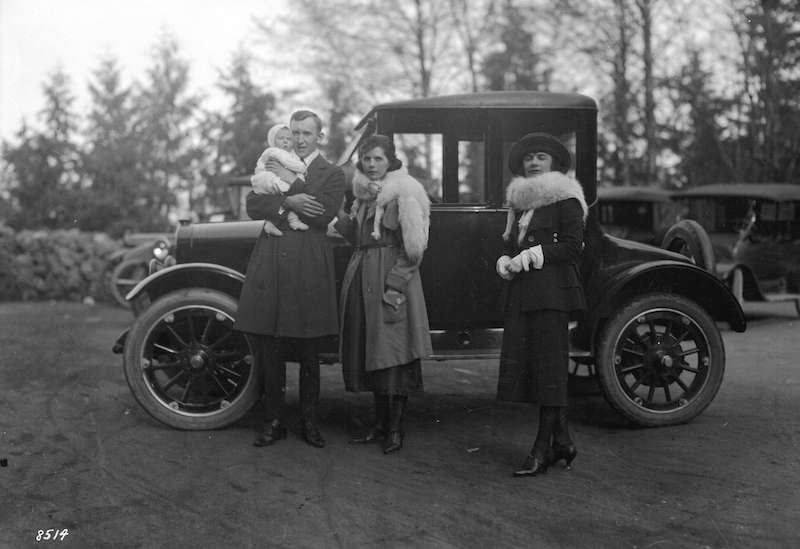 1920-Man, baby and two women posing beside car