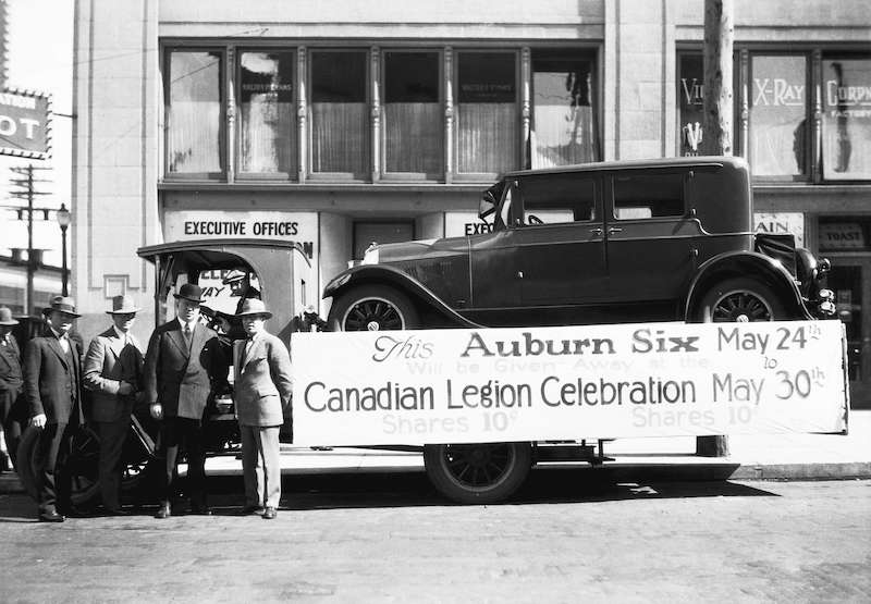 1927-Car on flatbed truck, banner reads This Auburn Six will be given away at the Canadian Legion celebration May 24 to May 30, shares 10 cents