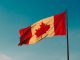 Canadian flag blowing in the wind with a blue sky background.