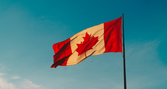 Canadian flag blowing in the wind with a blue sky background.