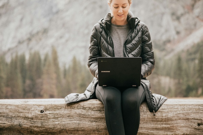 Woman using a laptop outside with nature in the background.