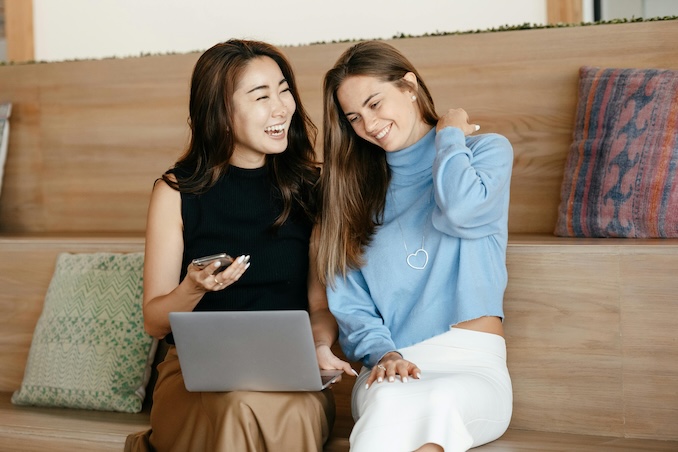 Two women laughing while using their laptop