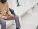 man using a cell phone while sitting on a ledge outside. featured image